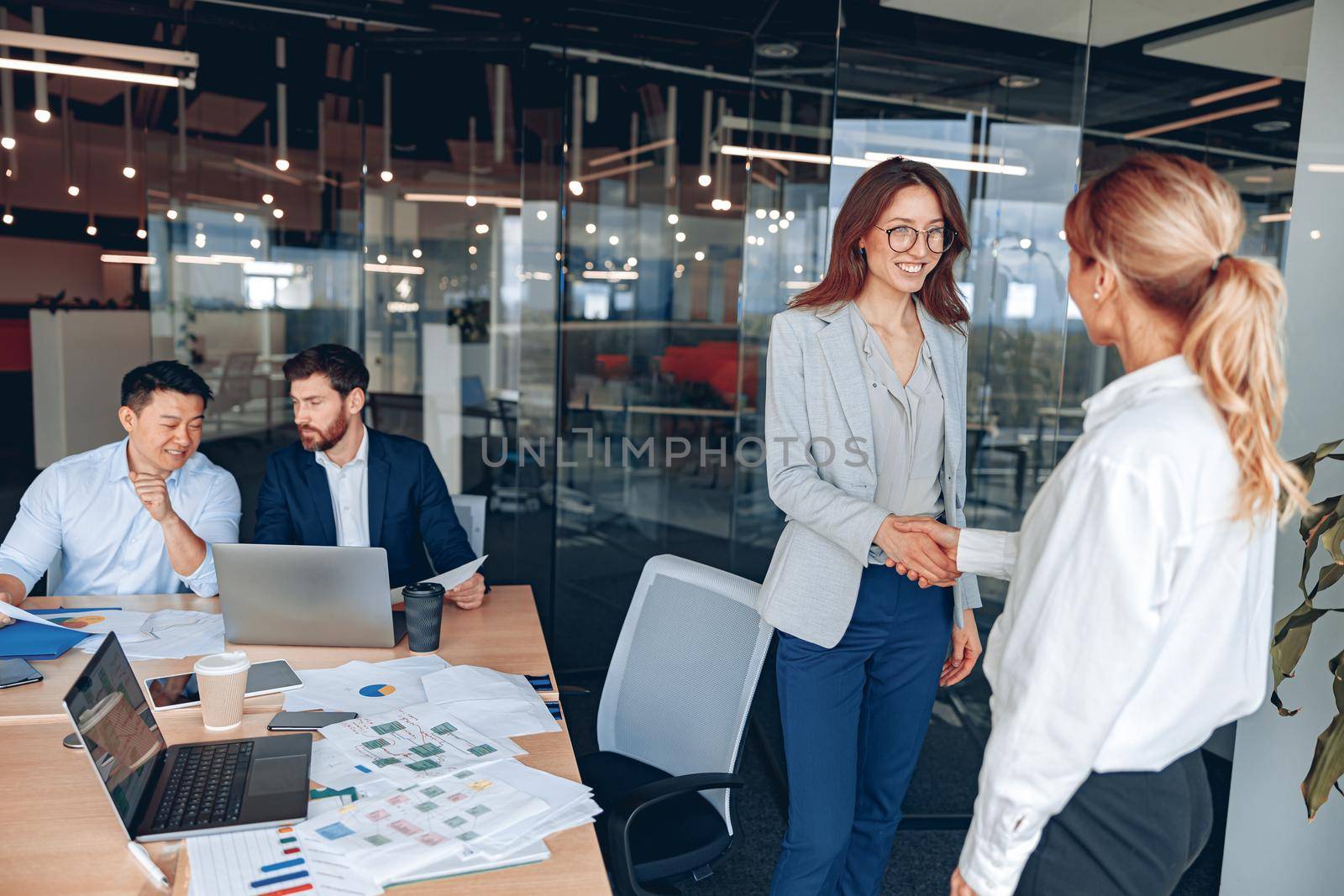 two smiling female workers are shaking their hands in modern office during meeting