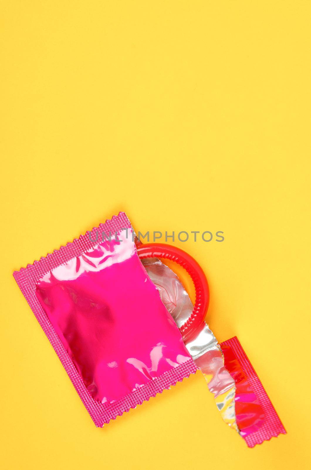 Pink opened condom and condom in pack on a yellow background. by Gamjai