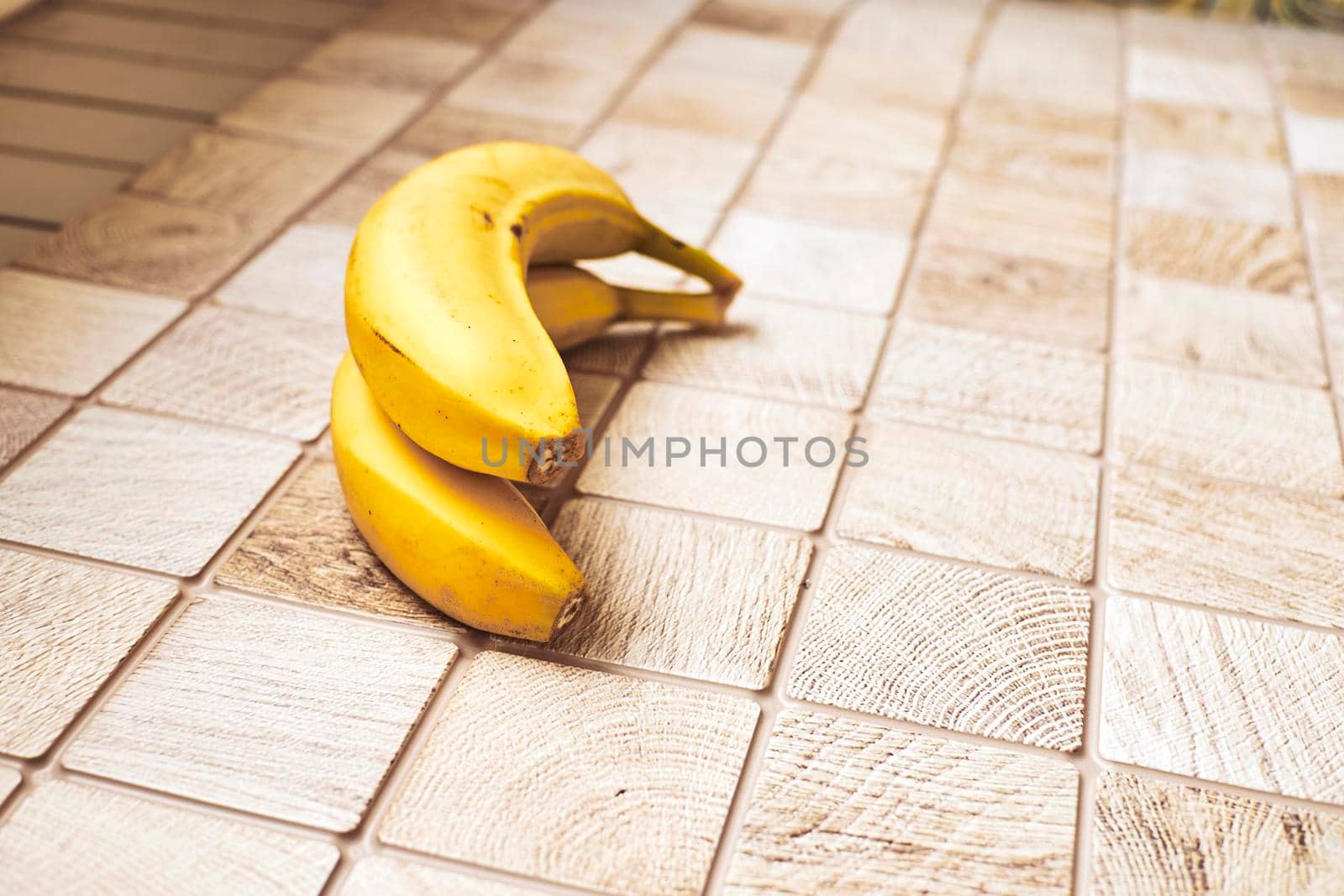 a long curved fruit which grows in clusters and has soft pulpy flesh and yellow skin when ripe.Two ripe bananas on a checkered wooden surface.