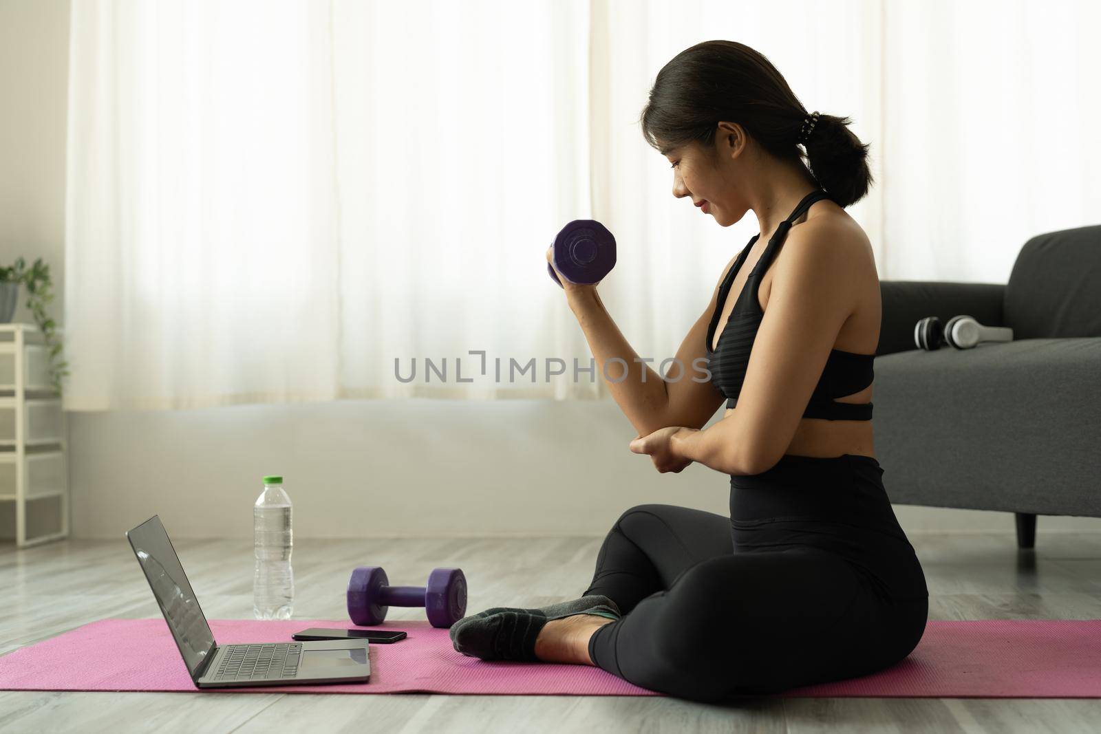 Young asian woman doing fitness exercises at home through virtual class by nateemee