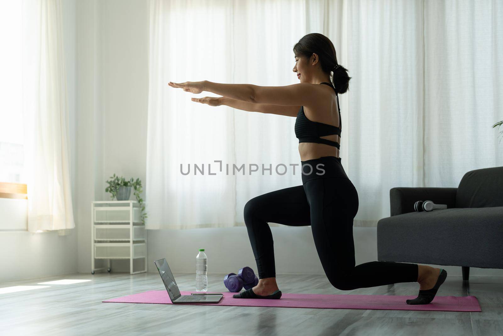 Fit sporty young asian woman online workout exercise at home. Active healthy girl enjoy sport pilates yoga fitness training on laptop computer stretching on yoga mat watching video class.