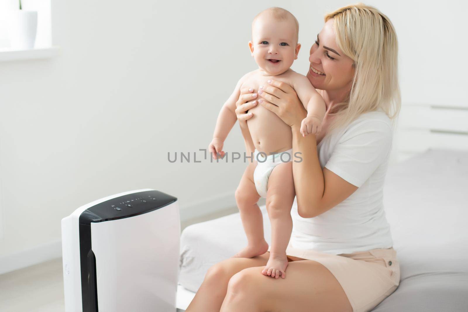 mother and baby near air purifier at home. by Andelov13