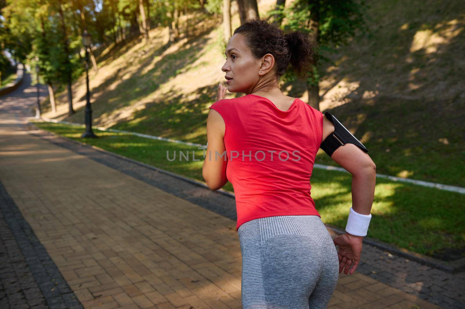Rear view of an African American woman running on the city park treadmill, enjoying outdoor workout and fitness functional training on a warm sunny summer day. Keep your body fit.