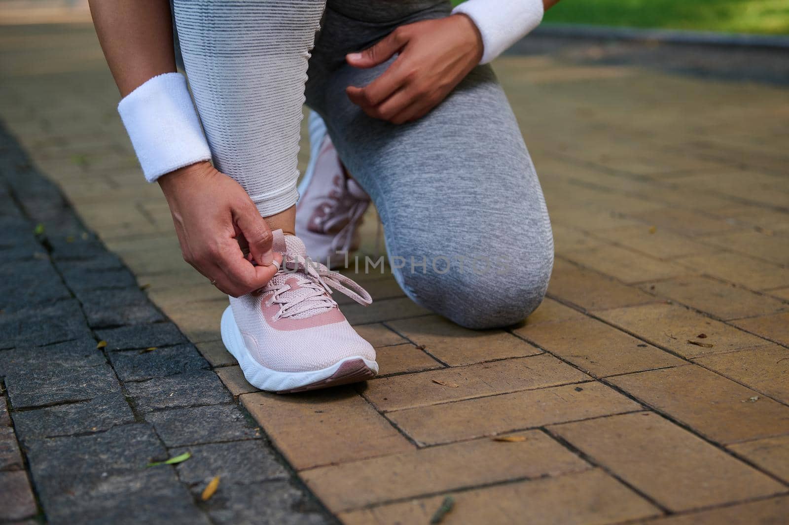 Cropped view of a female athlete, runner tying shoelaces on her sneakers getting ready for jog along the treadmill of a city park. Sport, active lifestyle concept