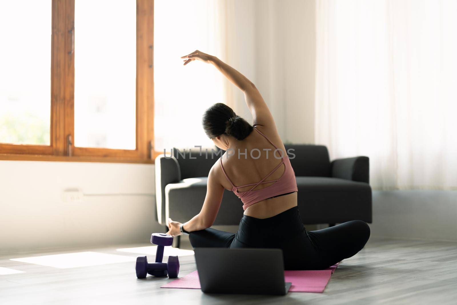 Young attractive woman practicing yoga in online yoga class on mat floors tanding in Full Version of Vasisthasana exercise, Side Plank pose, working out, pink sportswear