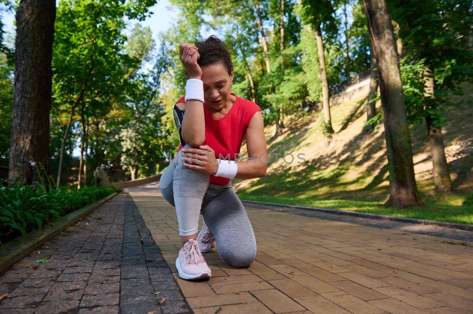 Exhausted sportswoman, female runner feels pain in her knee while running on a path in a forest park. Sports injury, knee pain,sport concept.