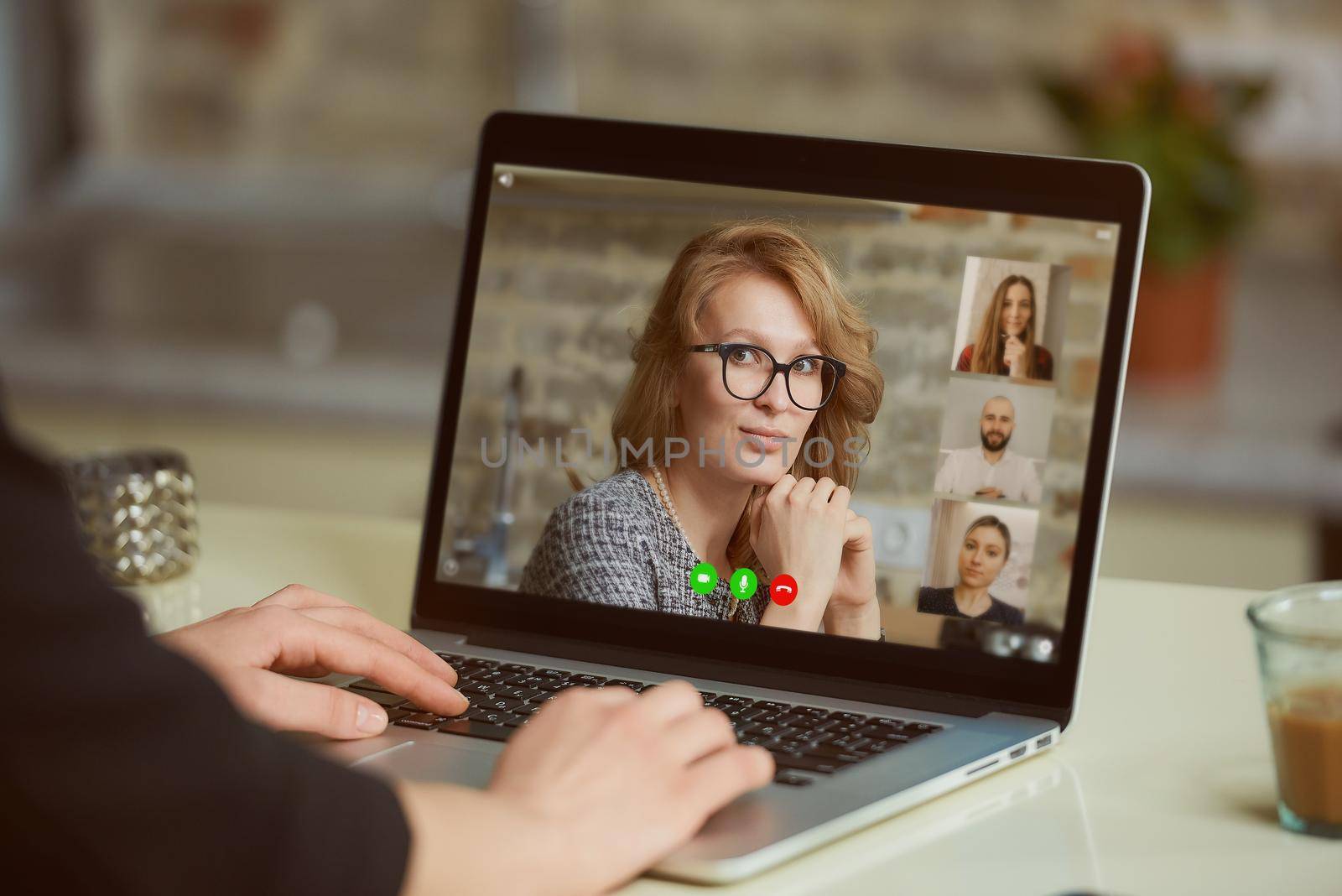 A laptop screen view over a woman's shoulder. A lady is discussing business with her colleagues on an online briefing on a computer in her apartment. A student on a video meeting on a computer.