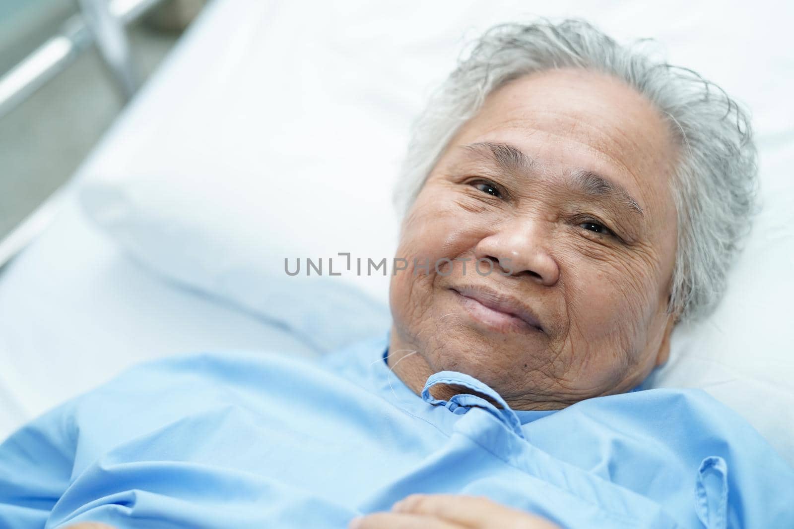 Asian senior or elderly old lady woman patient smile bright face with strong health while lying on bed in nursing hospital ward : healthy strong medical concept by pamai