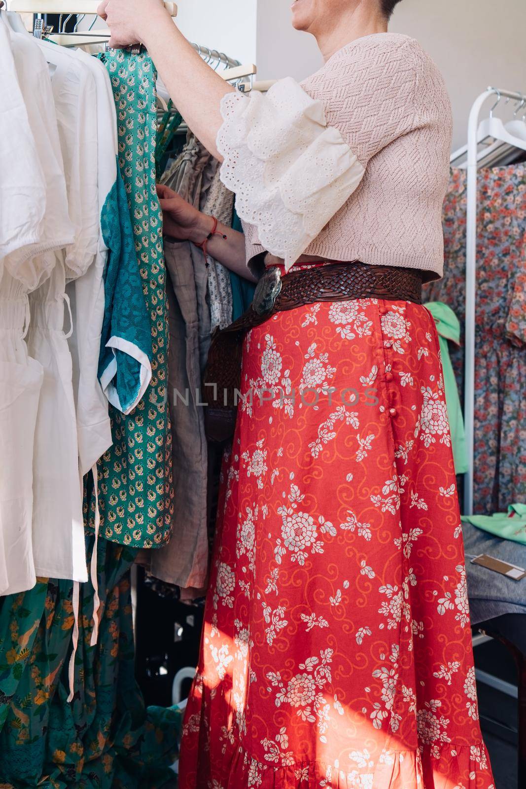 cropped shot of a woman picking up and buying clothes in a fashion shop. concept of shopping.concept of leisure. natural light from the shop window, sun rays, display with clothes, clothes rack, shop window, clothes, vertical