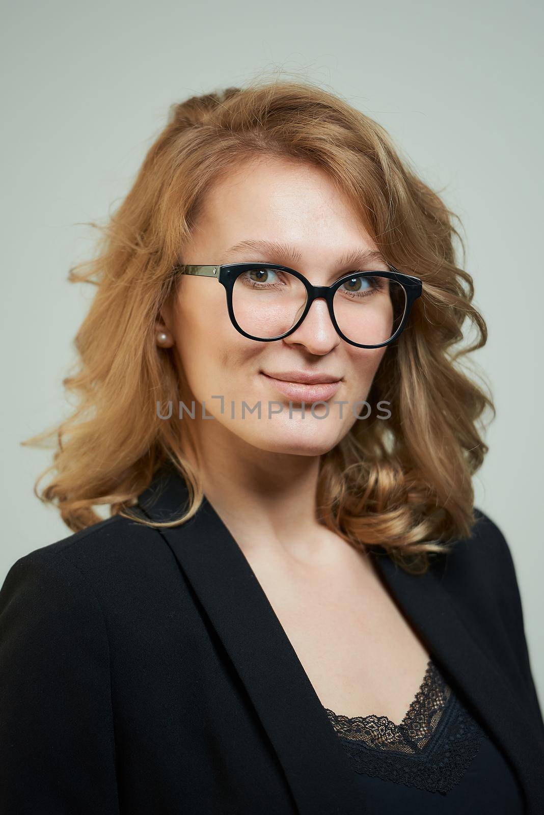 A stylish young woman in glasses dressed in a black suit with a black shirt. A close-up portrait of a happy blond lady who wears a business outfit. A concept of an office style wardrobe.