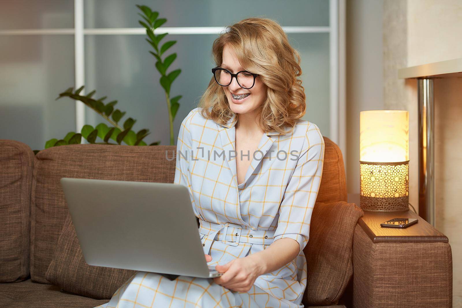 A woman in glasses works remotely on a laptop in her apartment. A girl laughing during a video conference with her colleagues at home. A female student with braces listening to an online lecture.