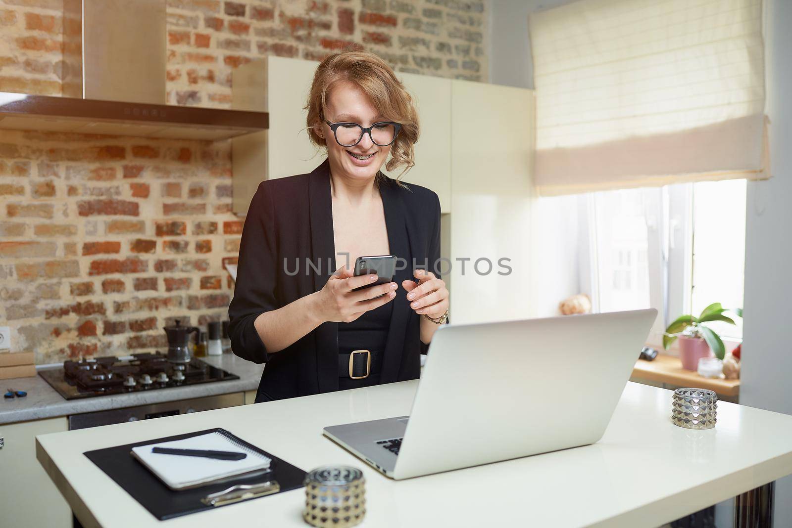 A blond woman in glasses works remotely in her kitchen. A happy girl with braces browses news on the internet with her smartphone at home. A teacher with a smile texting to her remote students.