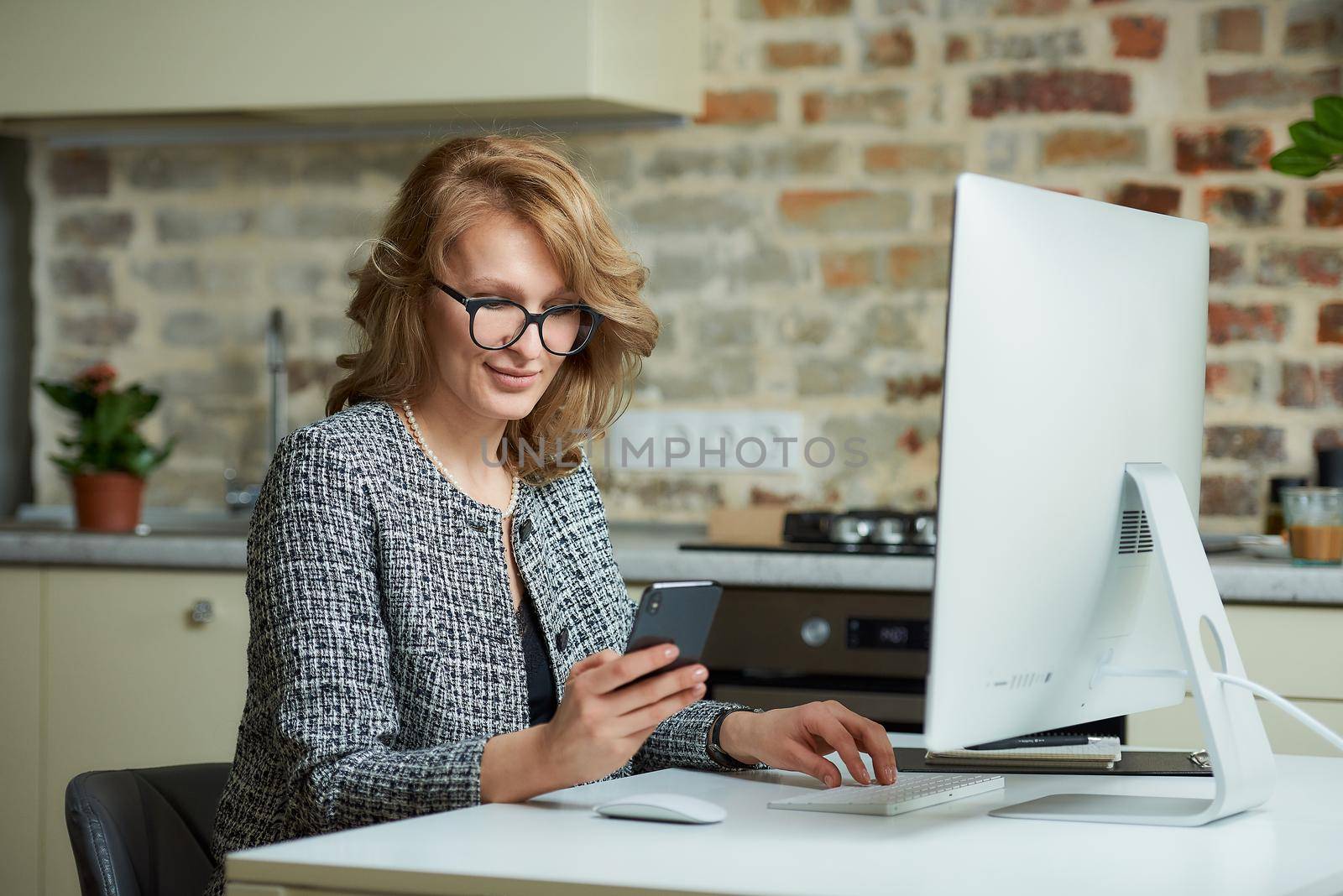 A woman in glasses works remotely on a desktop computer in her studio. A boss distracted by a smartphone during a video conference at home. A happy professor uses a cellphone before an online lecture.