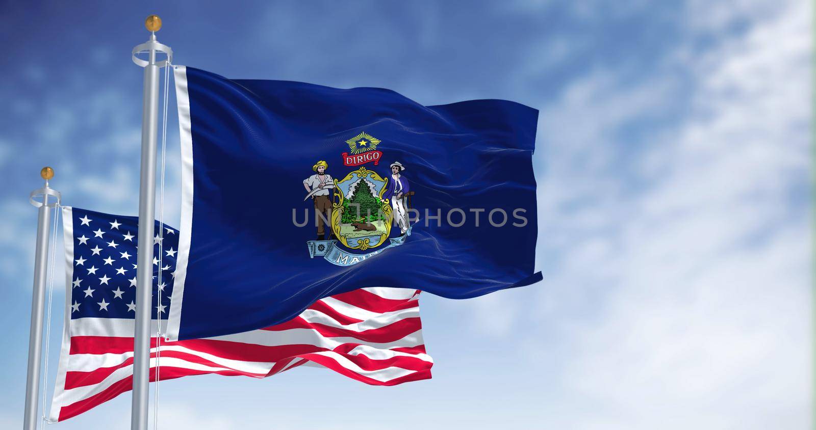 The Maine state flag waving along with the national flag of the United States of America. In the background there is a clear sky. Maine is a state in the New England region of the United States