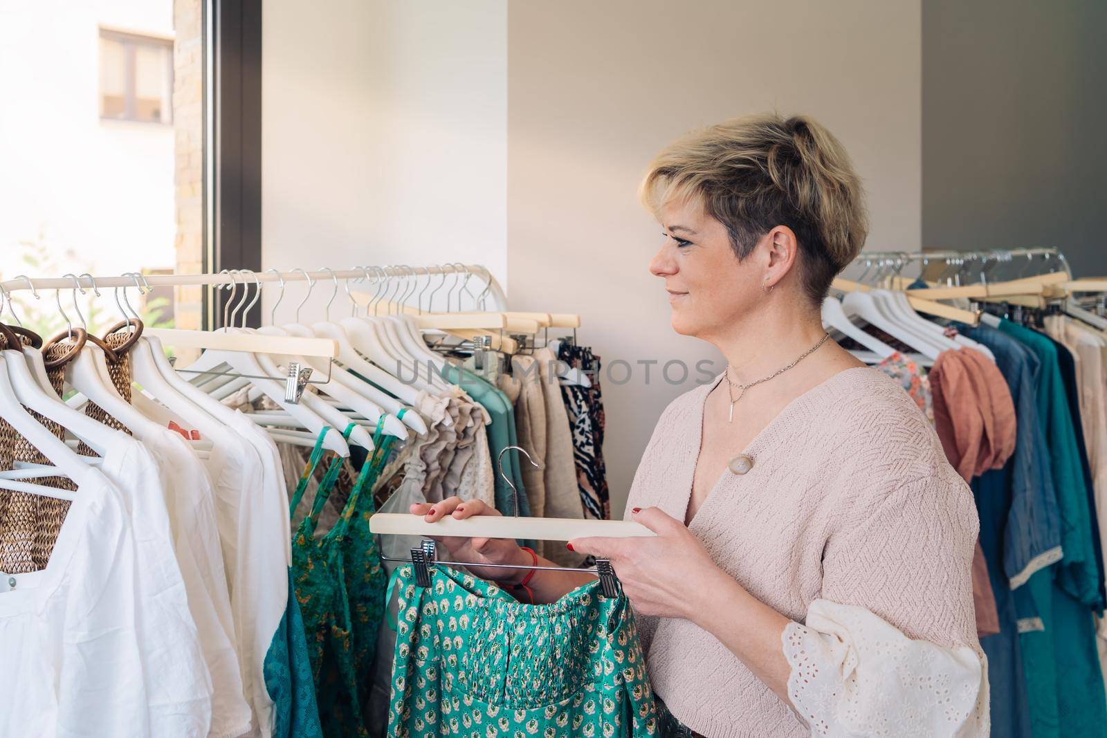 Modern mature woman looking at clothes to buy, in a fashion shop. shopping concept. by CatPhotography