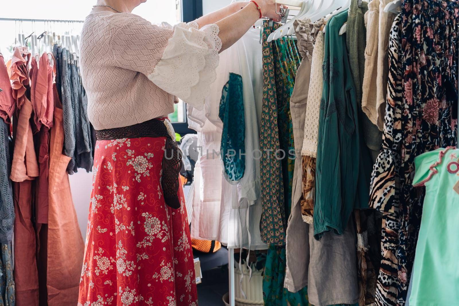 cropped shott of a woman picking up and buying clothes in a fashion shop. concept of shopping. concept of leisure. natural light from the shop window, sun rays, display with clothes, clothes rack, shop window, clothes, Horizontal.