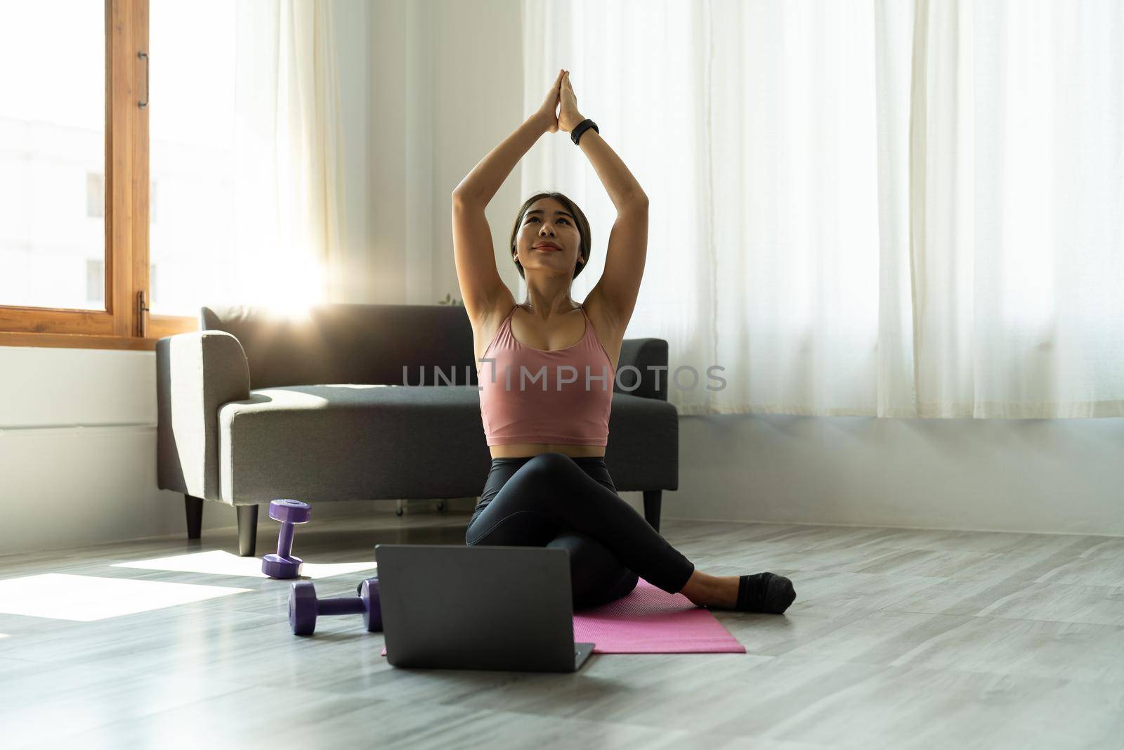 Calm relaxed young asian woman sitting in lotus position with hands up namaste gesture, closed eyes, breathing, resting, deeply meditating, practicing yoga on yoga mat at home by nateemee