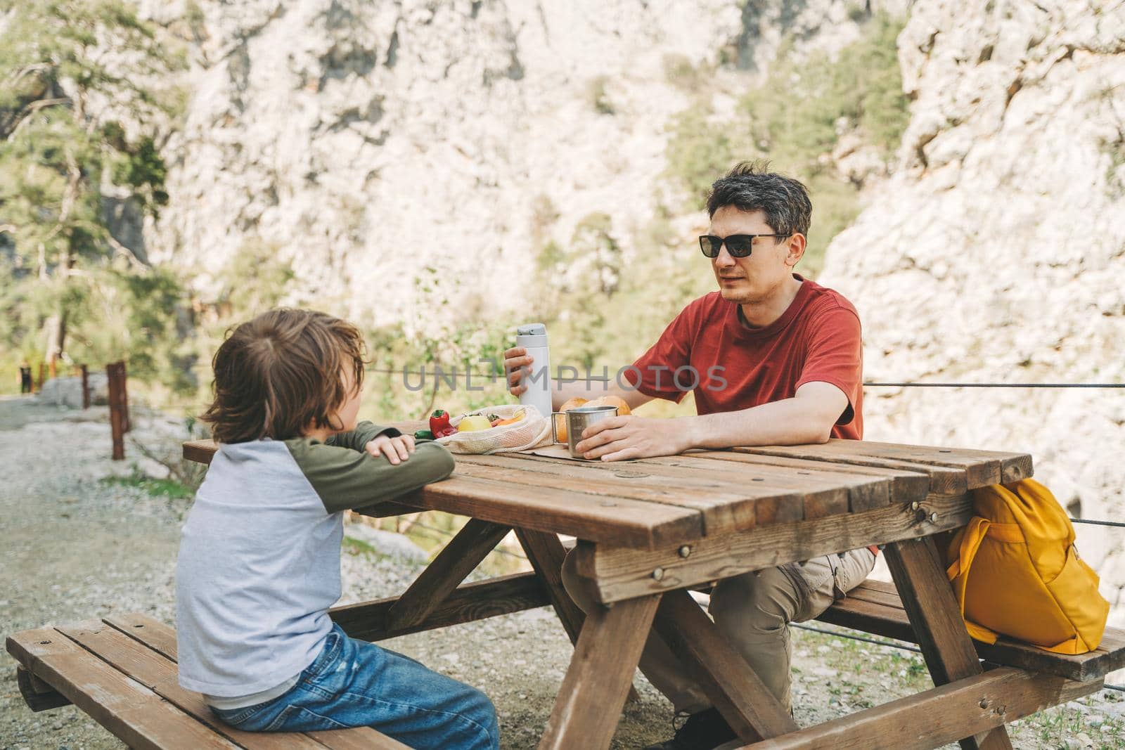 Close-up view of father and his school boy son on a family picnic in the mountains. Child kid and his dad taking a rest and enjoying a picnic while hiking in the mountains.