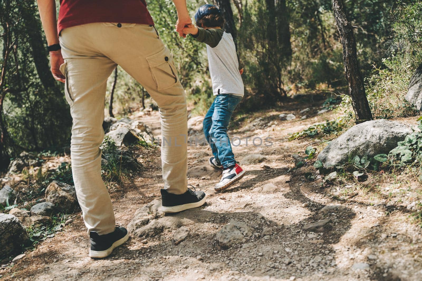Close-up rear view of tourists school boy and his dad walking a stone footpath in spring forest. Child kid and father wearing casual clothes while hiking in summer greenwood forest.
