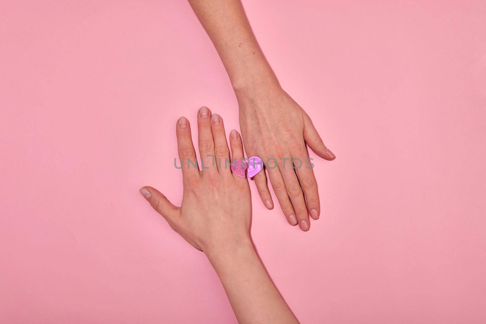 Unrecognizable couple forming heart with rings pink background by Demkat