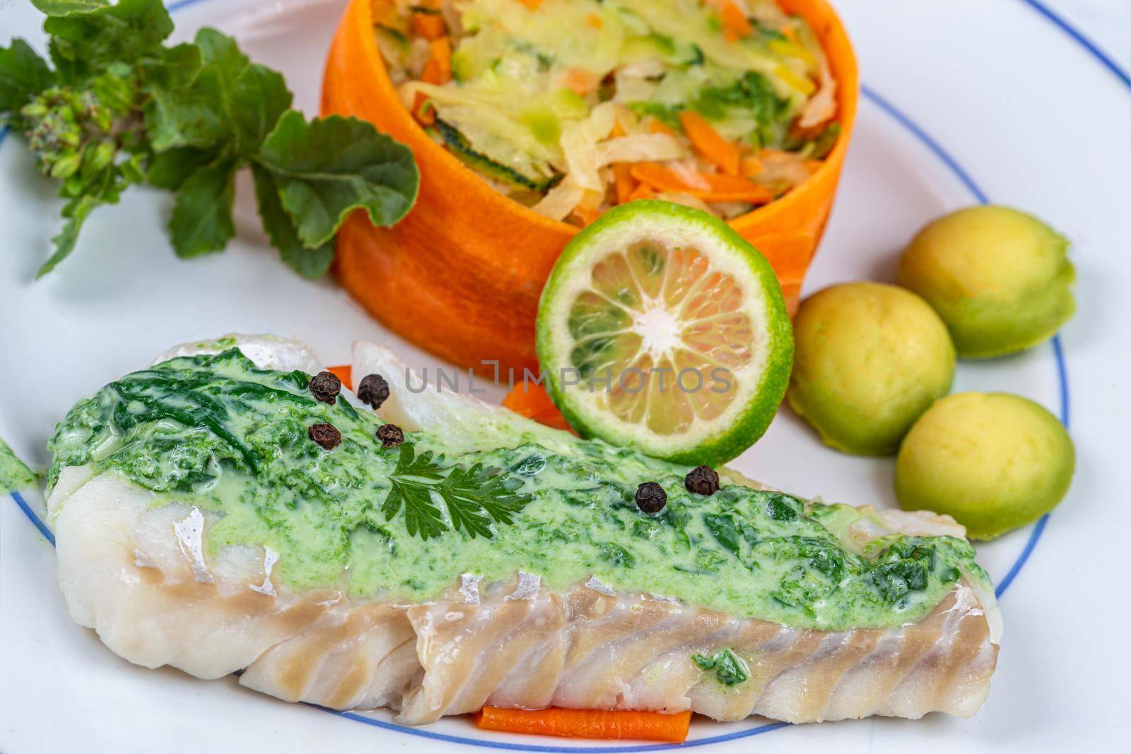 Cod back covered with sorrel sauce, accompanied by vegetables.