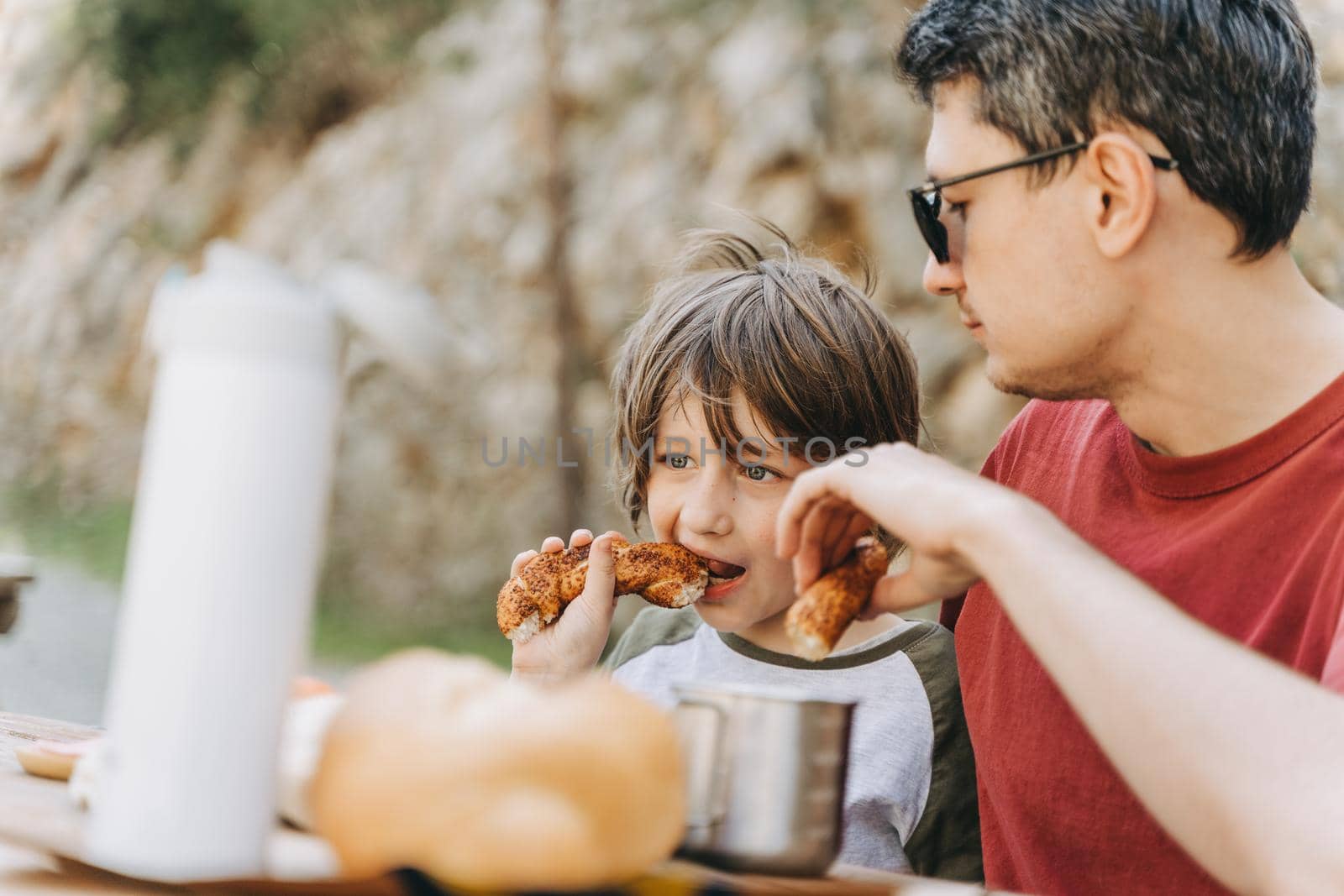 Close-up view of father hugs his school boy son on a family picnic in the mountains. Child kid and his dad taking a rest and enjoying a picnic while hiking in the mountains.