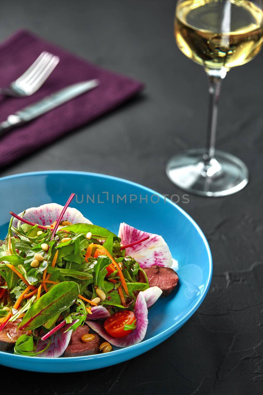 Spicy beef slices meat salad with tomatoes, parsley, radish and salad leaves spinach on black texture background table. Still life