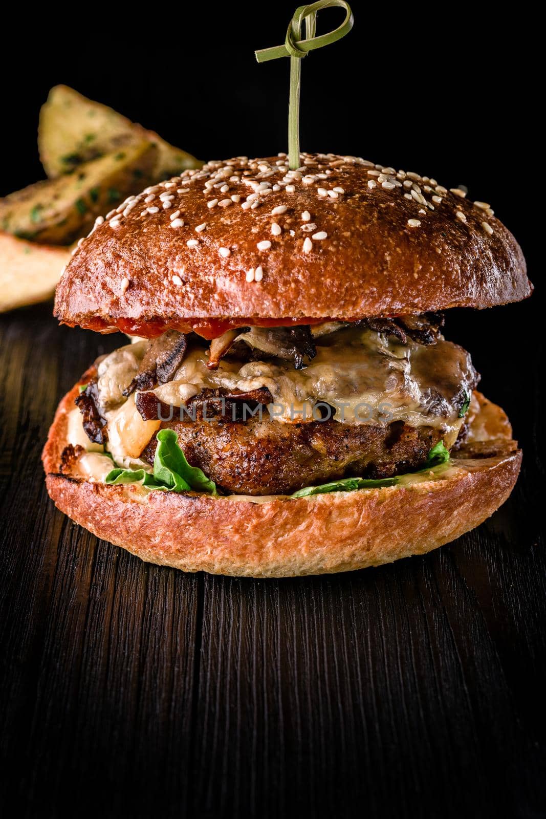 Cheese burger with grilled meat, cheese, tomato and potatoes on dark wooden surface. Fast food template. Real photo. Ideal for advertisement. Close-up. Still life hamburger