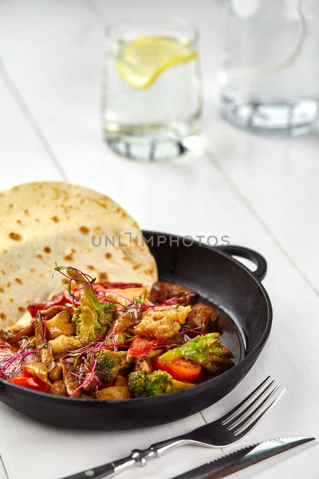 Roasted vegetables - potato, green beans, carrot and paprika in black iron plate on white wooden table. Vegetarian food. Diet menu. Still life