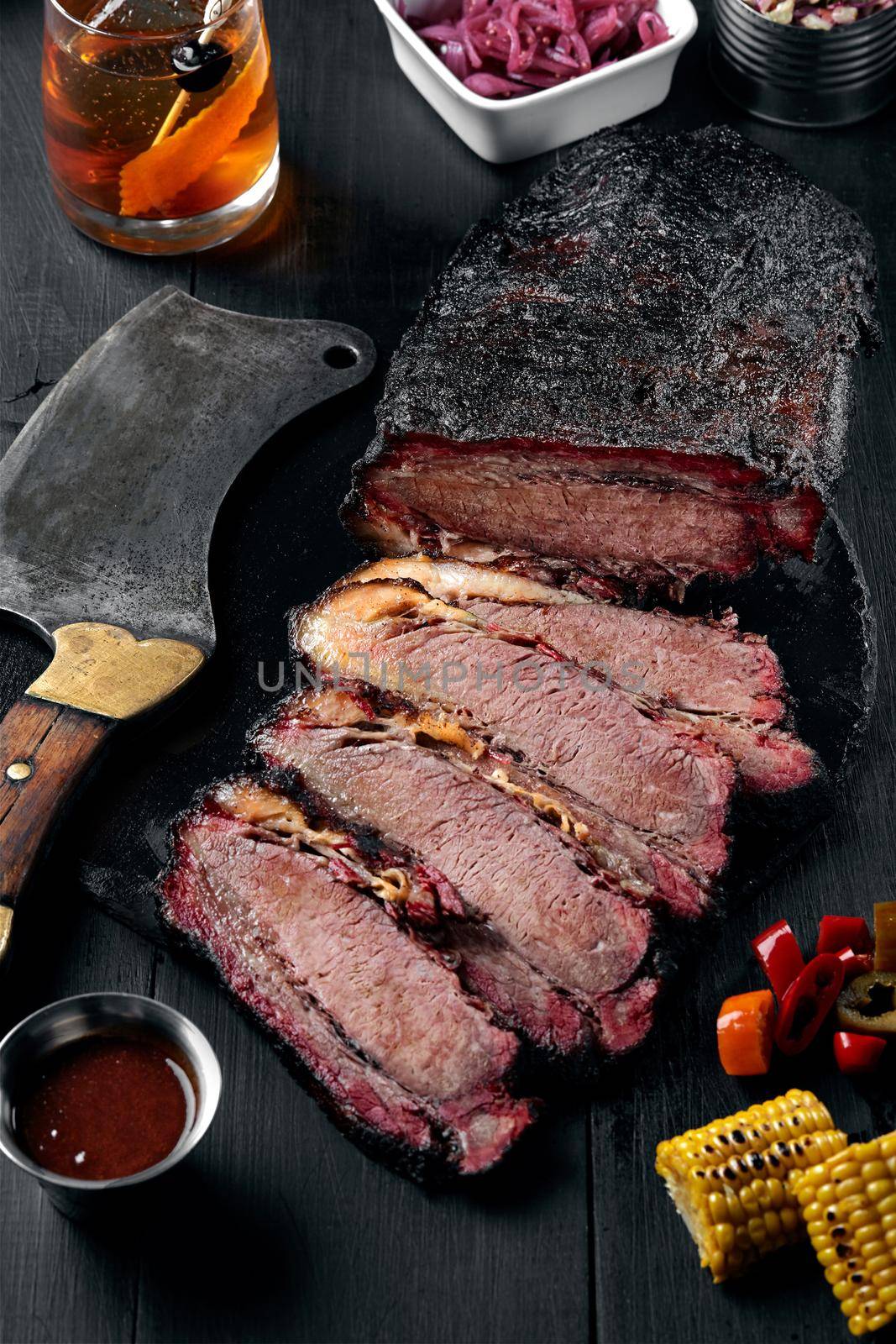 Fresh Brisket BBQ beef sliced for serving against a dark background with sauce, hot peppers and corn. Generous accommodation for copy space. American style
