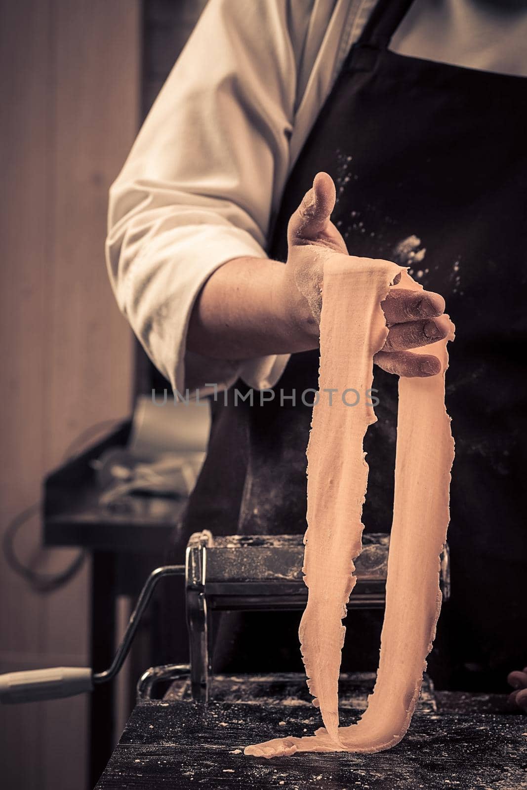 The chef makes fresh spaghetti from scratch. Wooden table. Photo in brown tones. Kitchen.