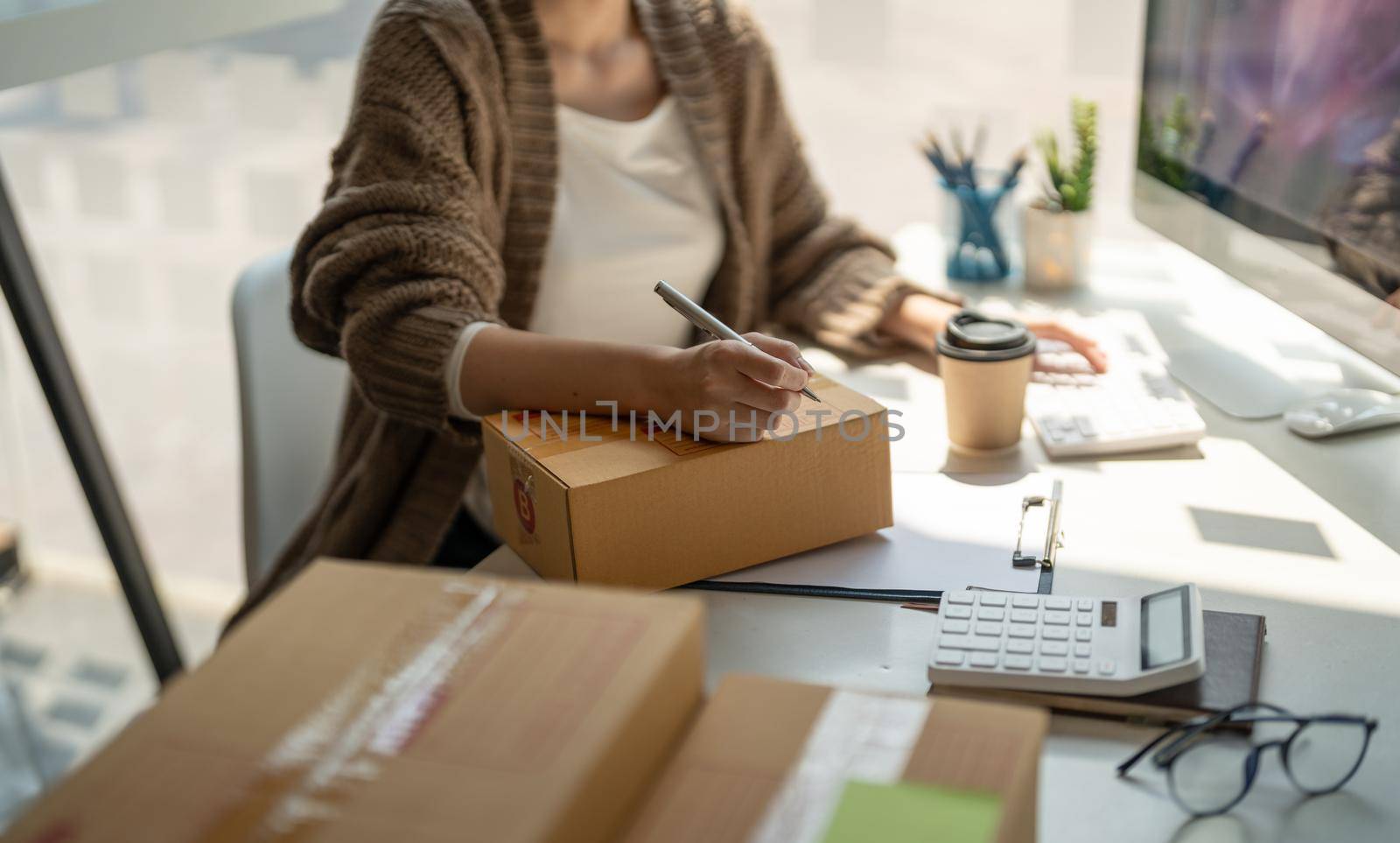 Online sales business woman owner is taking note of the customer's address on the parcel box being prepared for delivery.