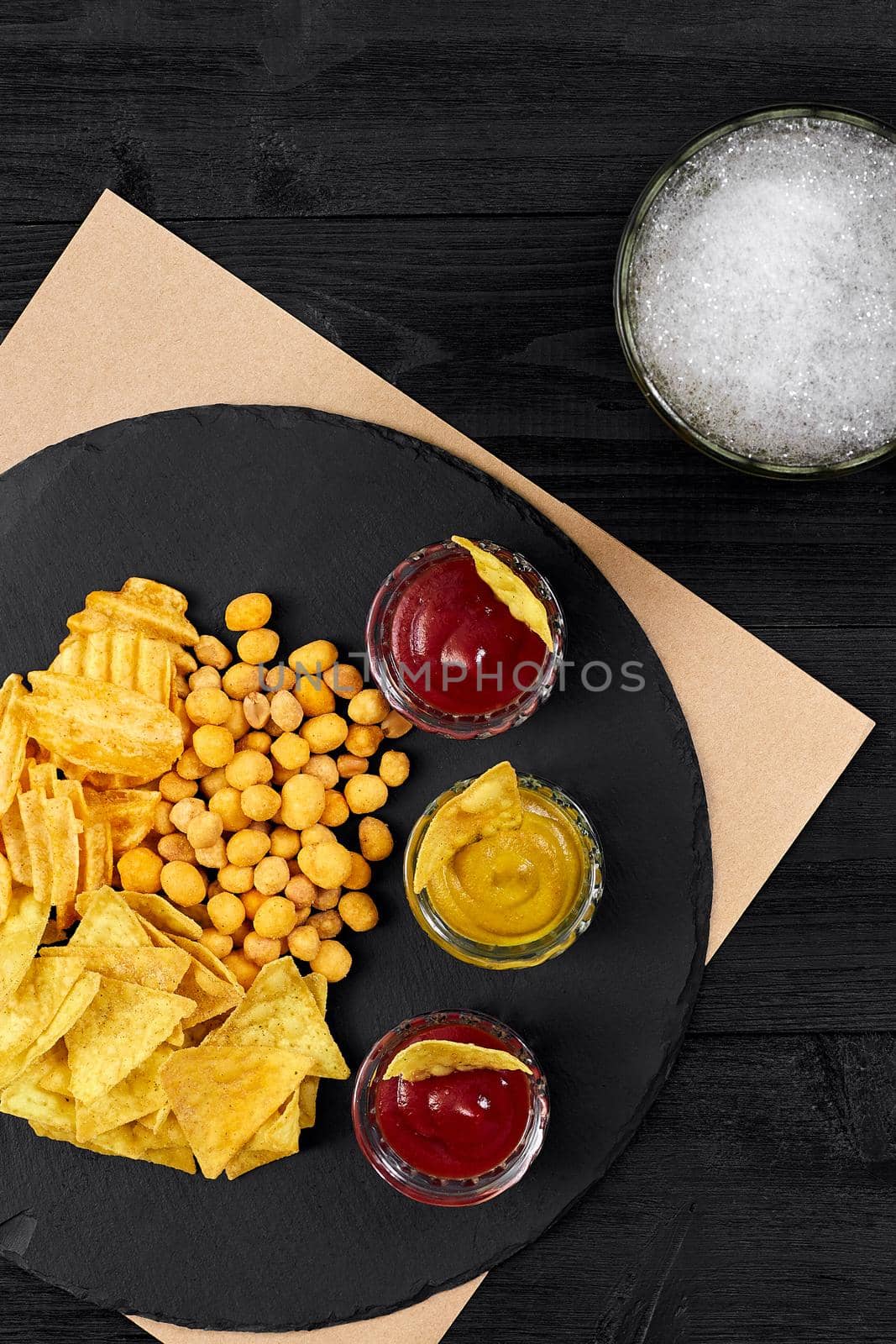 Overhead view of beer glass and snacks with sauce on black wooden table. by nazarovsergey