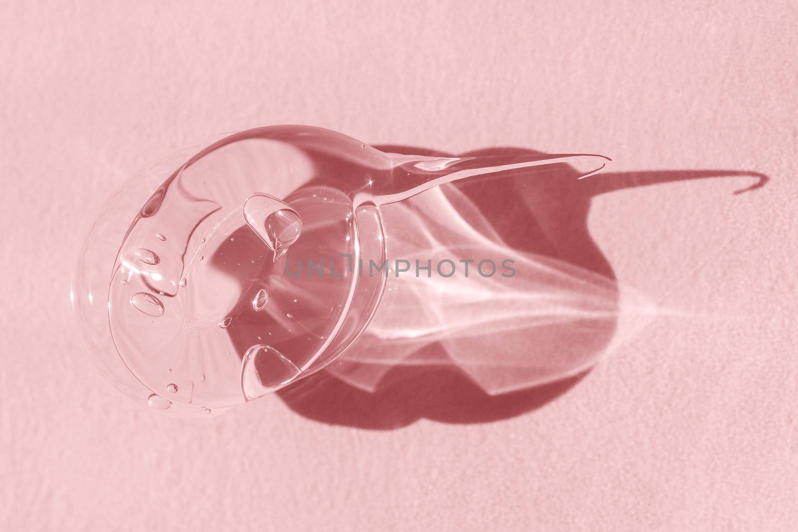 Transparent gel smear smudge swatch on pink backdrop with shadow. Styling gel lotion, aloe vera cleanser, shampoo drop. Macro of droplet of skincare product. by photolime