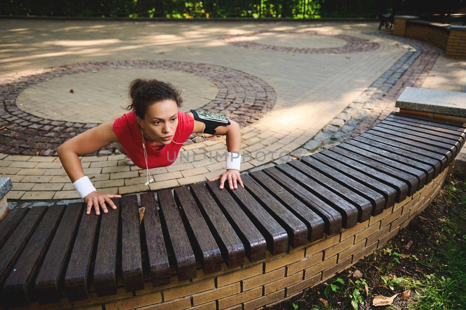 Determined active beautiful woman exercising outdoors,pushing ups from wooden bench while performing full body functional cross training outdoors. Sport, body weight training, weight loss concept