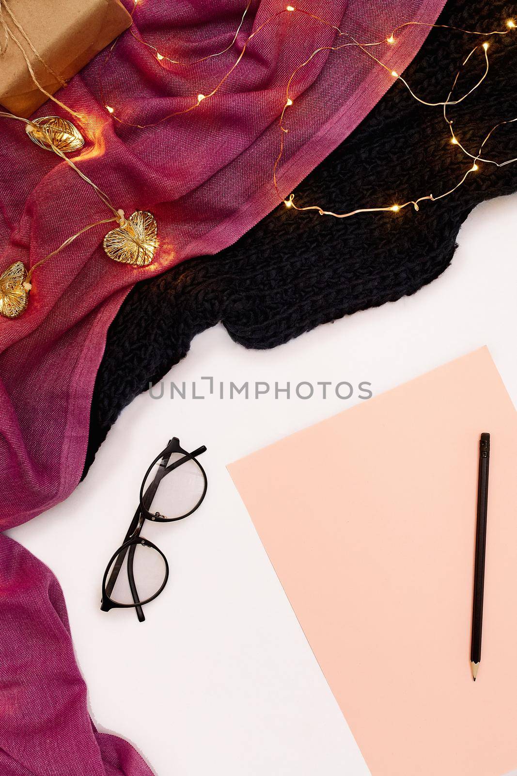 Black glasses, pink paper with new years goals. Scarf and Christmas lights on white background. by nazarovsergey