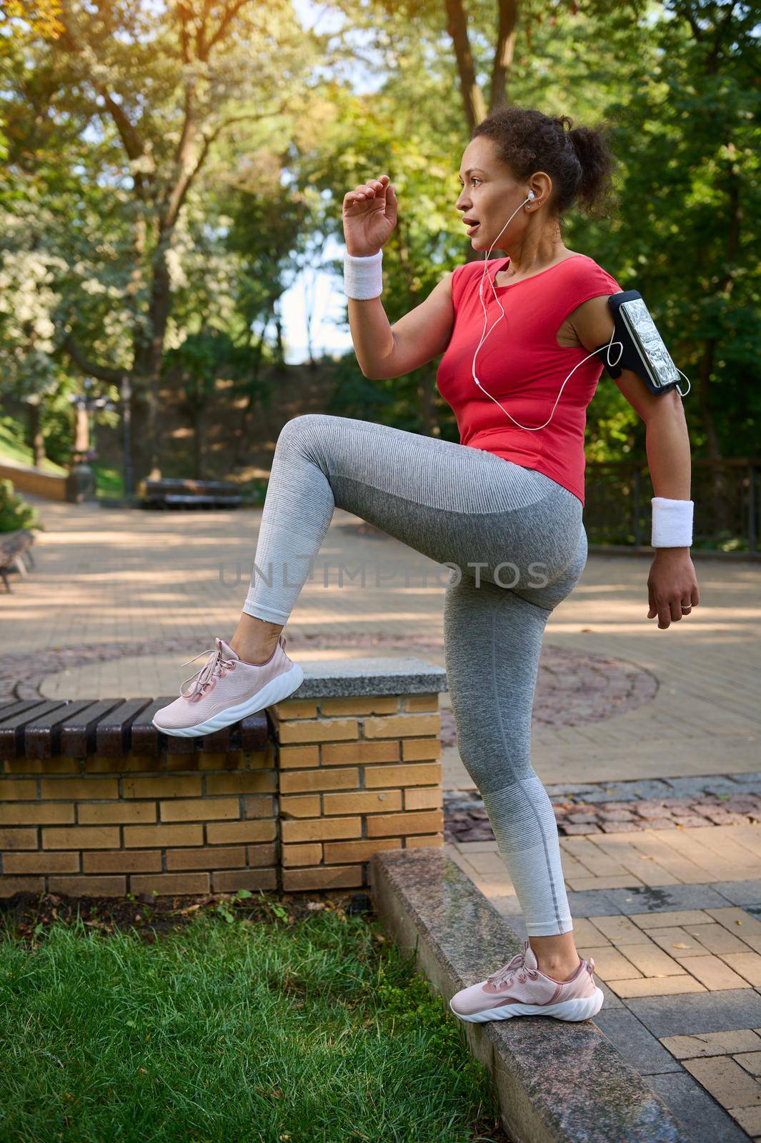 Full length of a charming middle aged female athlete exercising in the city park, doing legs exercises on stairs. Enjoy warm sunny days, keep your body fit. Fitness, sport and Active lifestyle concept