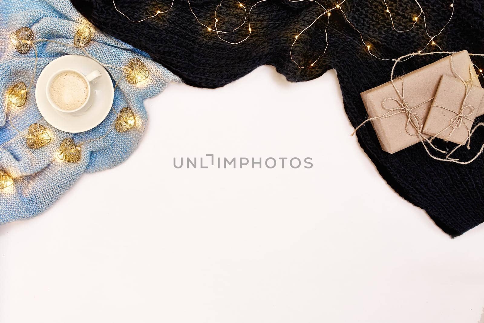 A cup of coffee with warm blue scarf and Christmas garland on white background. Top view. Flat lay. Copy space. Still life