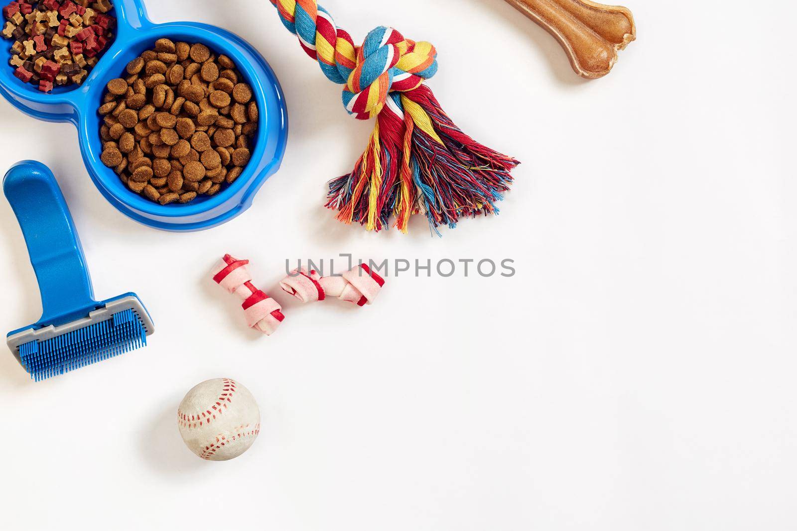 Dog care items, isolated on white background. Dry pet food in bowl, toy and bones. Top view. Copy space. Still life. Flat lay.