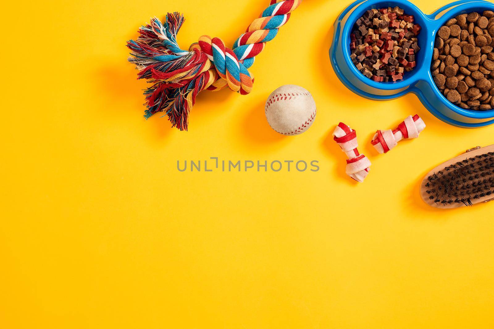 Toys -multi coloured rope, ball and dry food. Accessories for play on yellow background top view by nazarovsergey