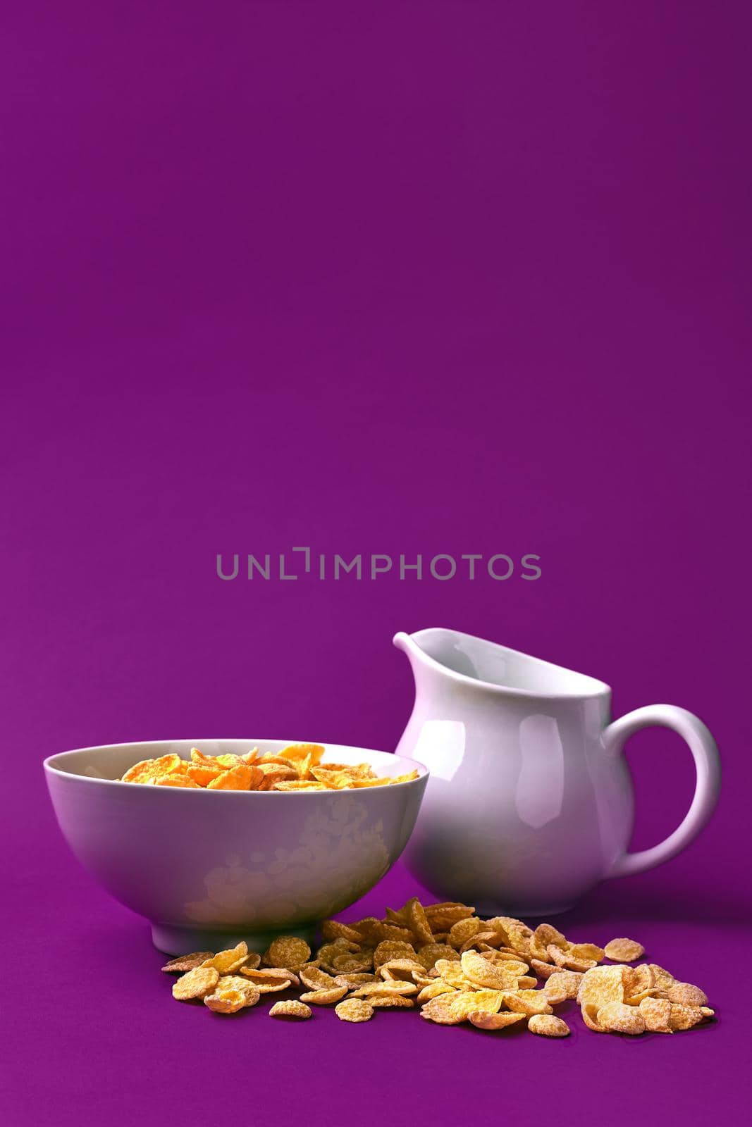 Bowl with corn flakes, jug of milk on purple background. oncept of a healthy breakfast. Copy space. Still life. Flat lay