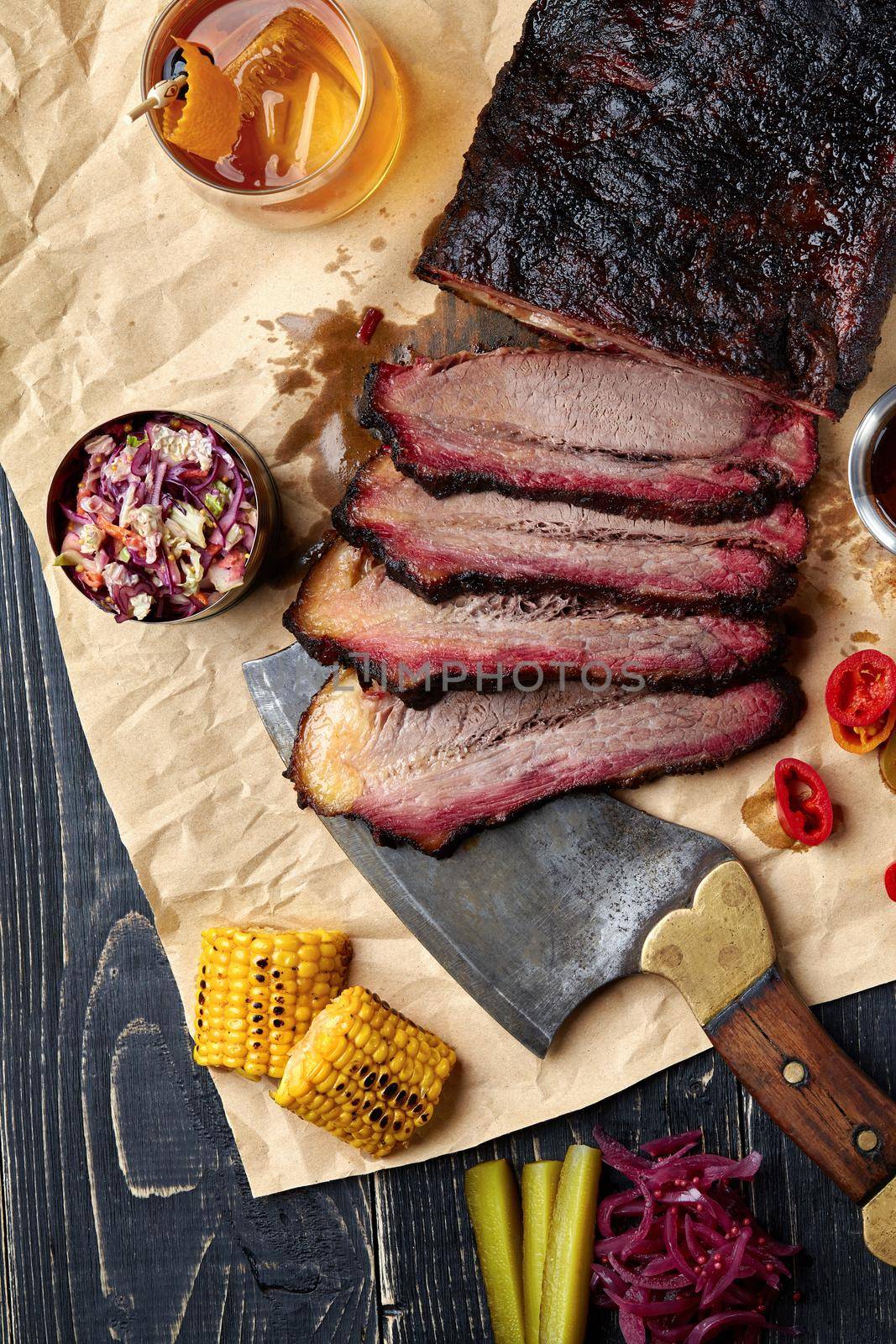 Fresh Brisket BBQ beef sliced for serving against a kraft paper background with sauce, hot peppers and corn. by nazarovsergey