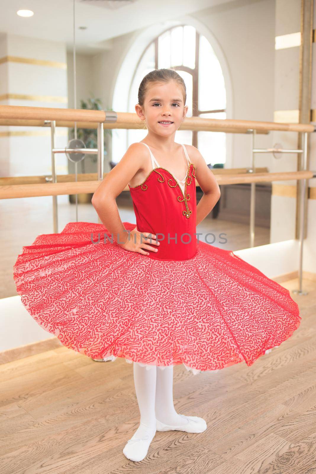 Full length portrait of a cute little ballerina in a performance dress in a dance hall with large mirrors by Nickstock