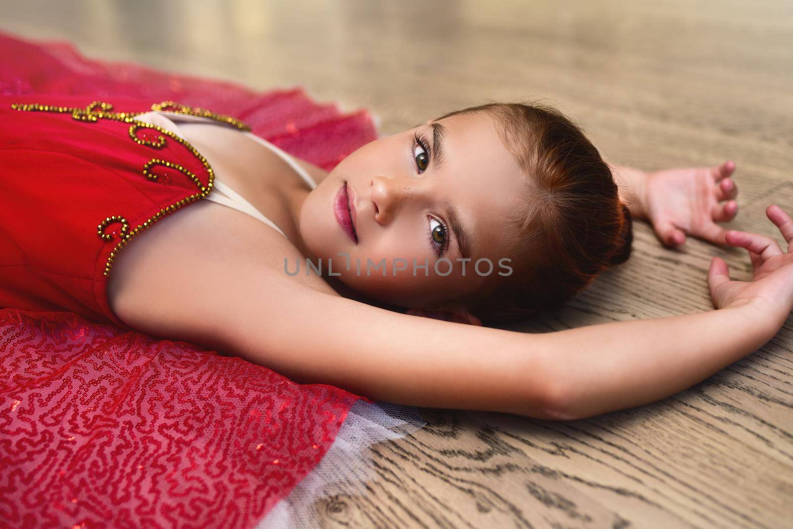 side view portrait of a cute Beautiful little ballerina in a performance dress lying on the floor of the dance hall