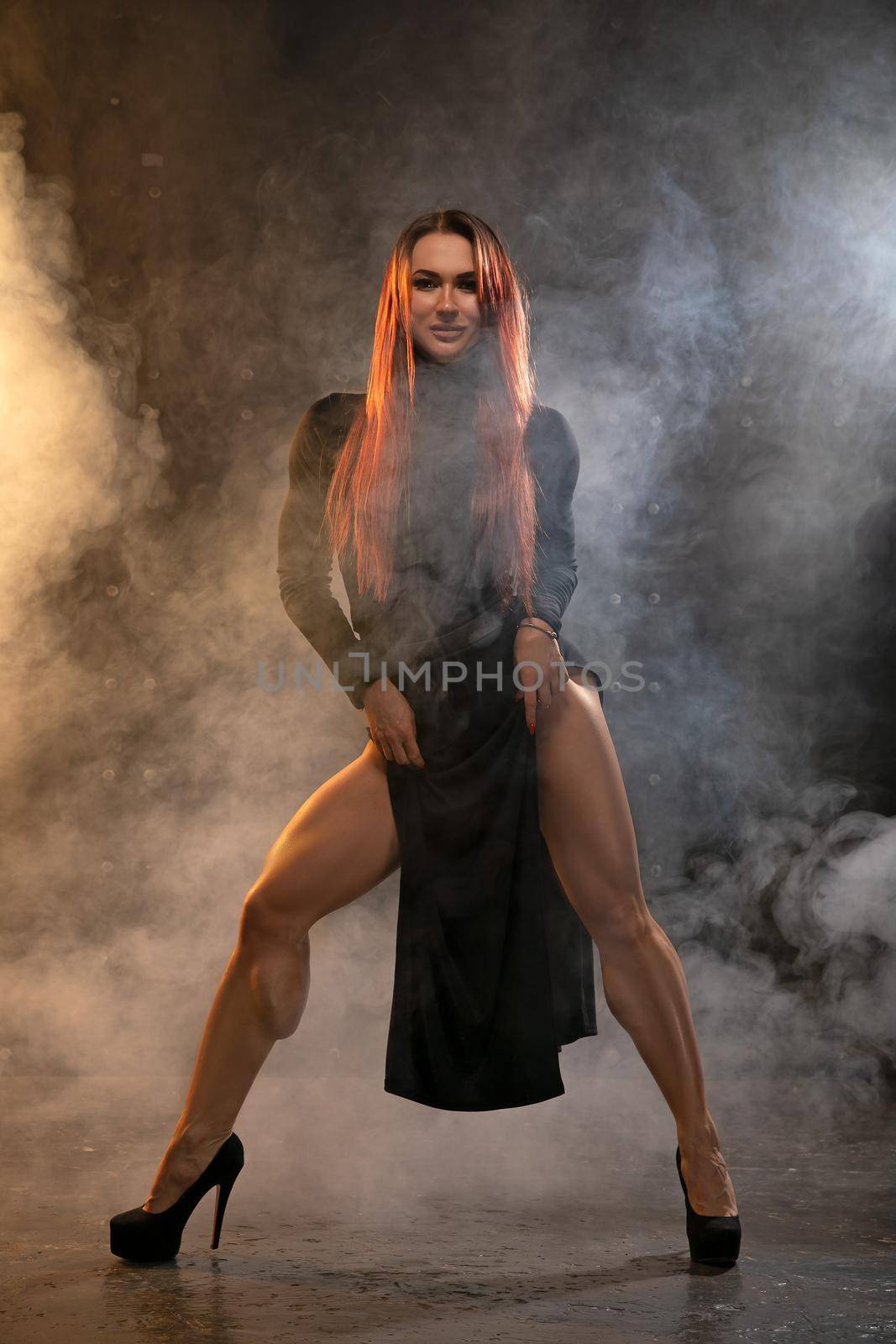 Attractive redhead girl in black dress demonstrates athletic legs in the smoke