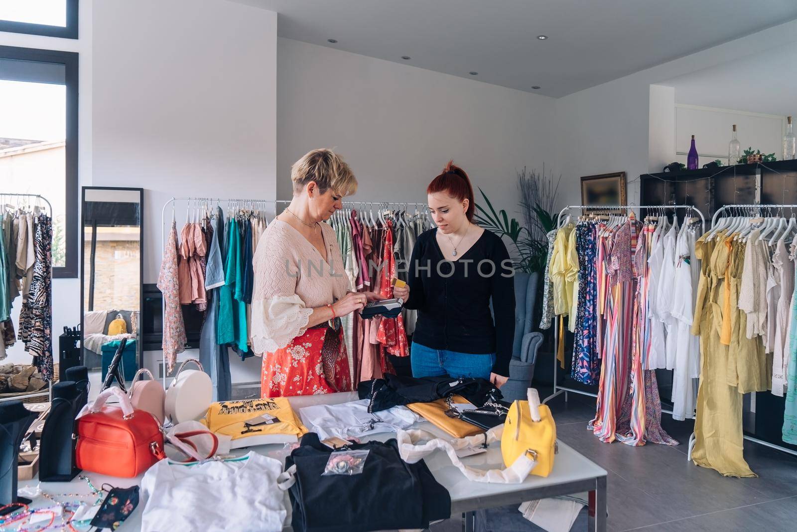 clothing shop assistant advising a customer on a purchase. young woman paying for clothes with a credit card. by CatPhotography