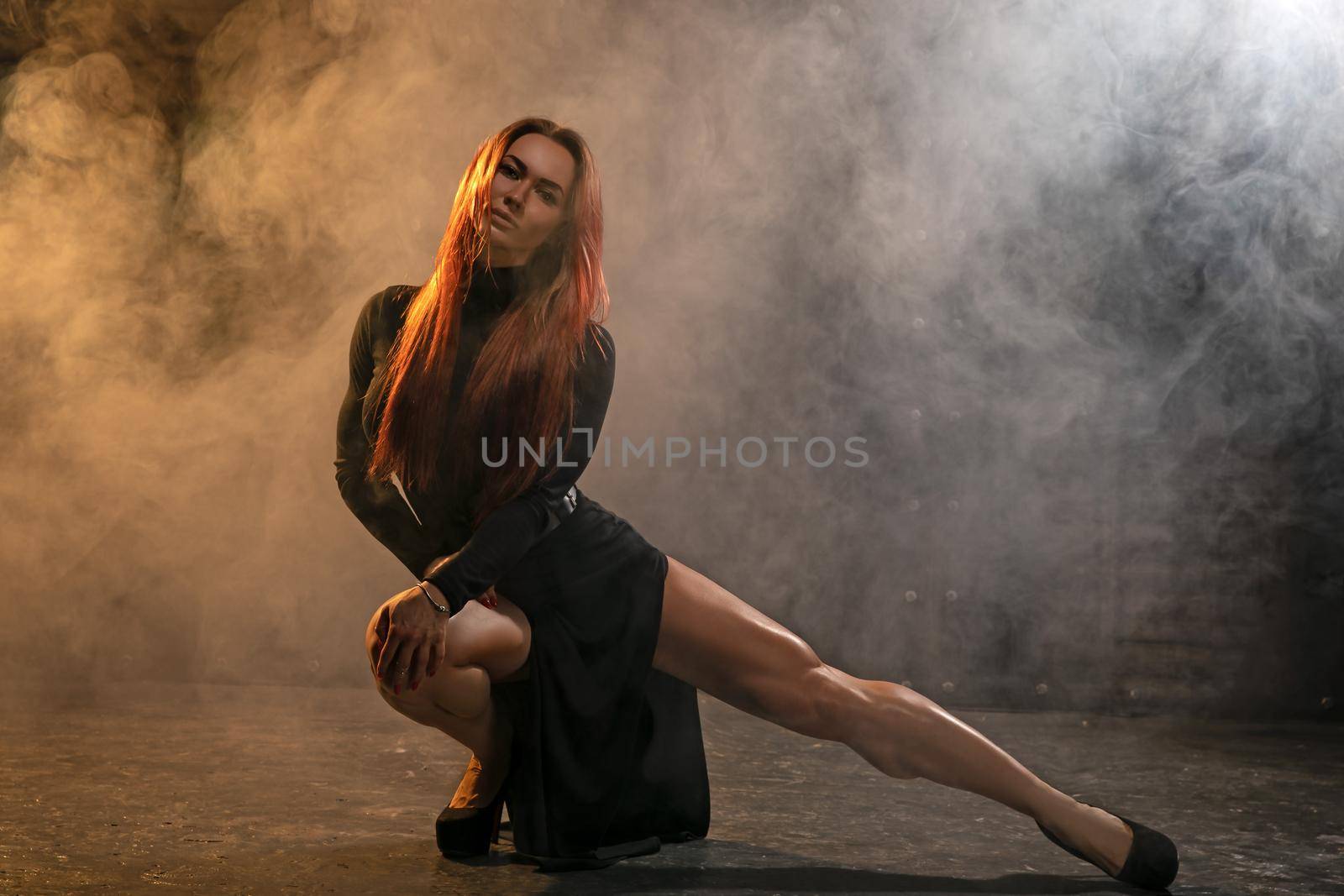 Attractive redhead girl in black dress demonstrates athletic legs in the smoke