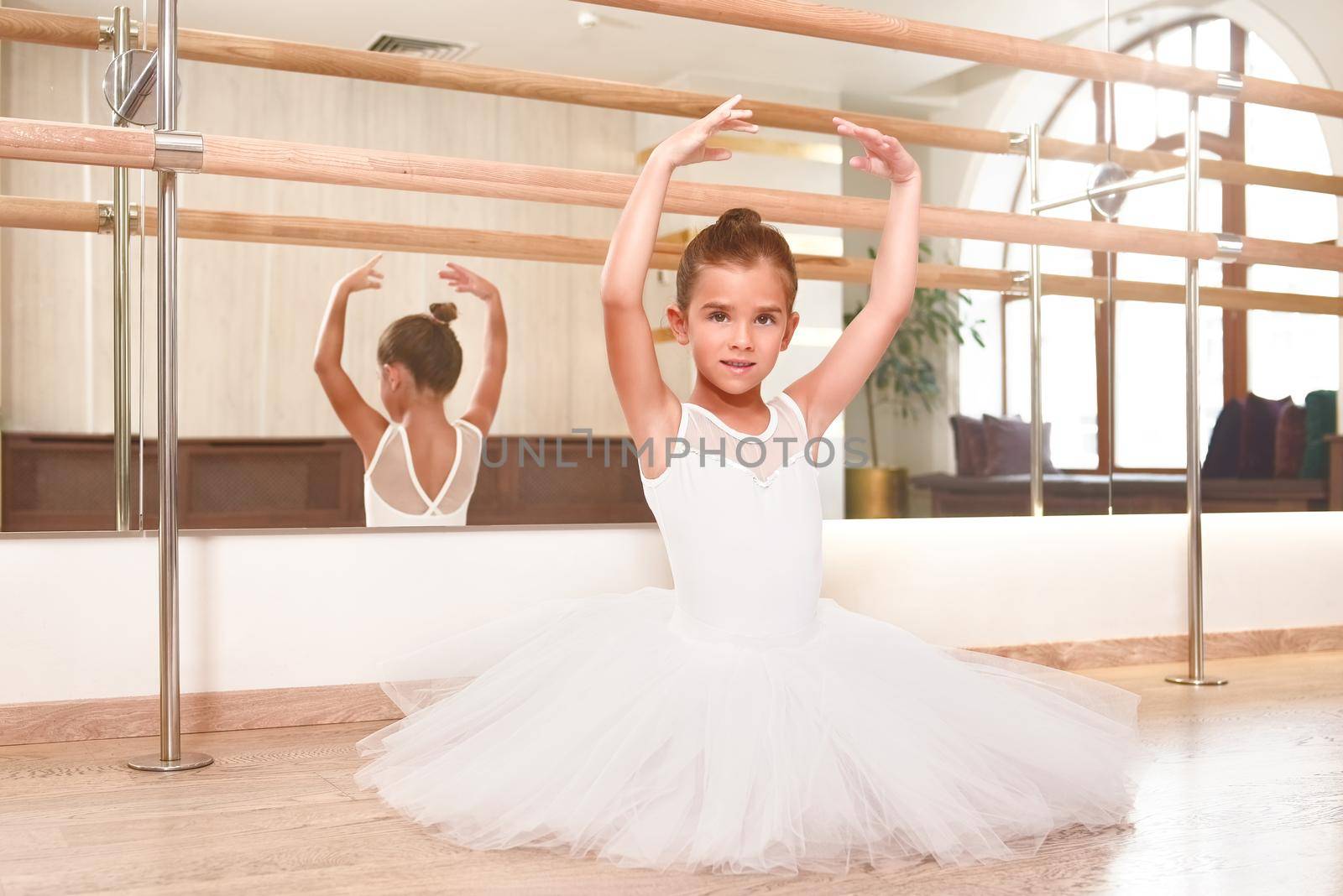 cute little ballerina standing with her hands up in a performance dress. She is dreaming to become a professional ballet dancer. Dance school, ballet studio. by Nickstock