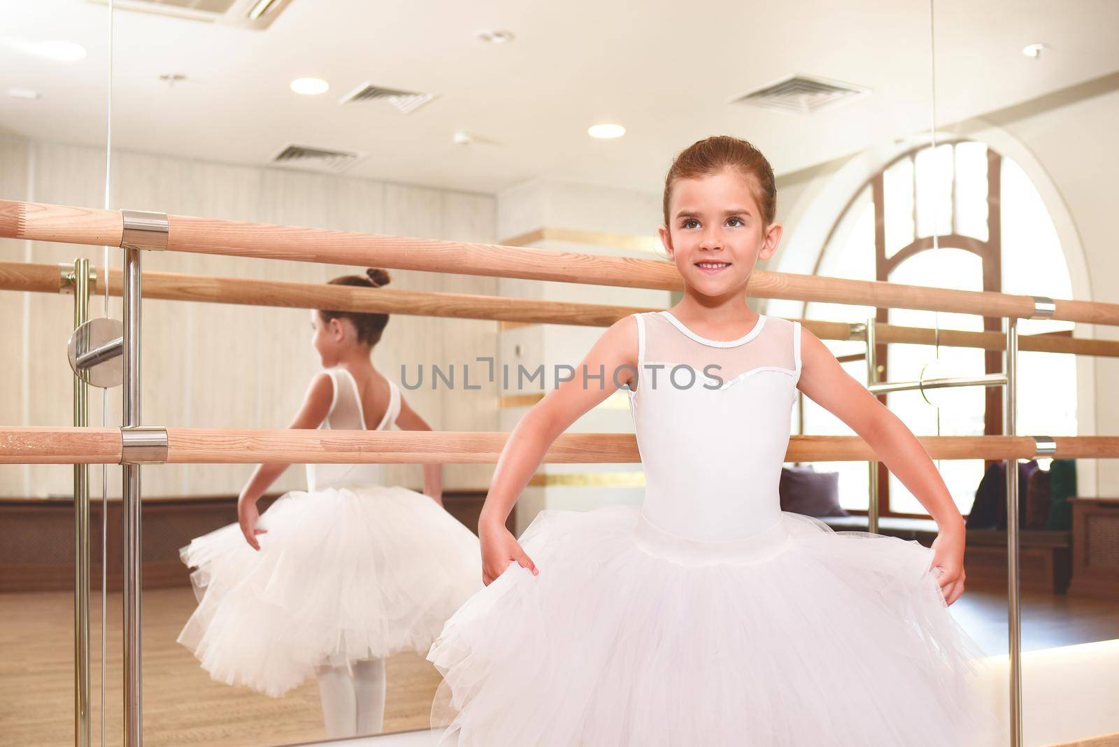 A cute little ballerina in a dance hall with large mirrors.she is ready to dance. by Nickstock