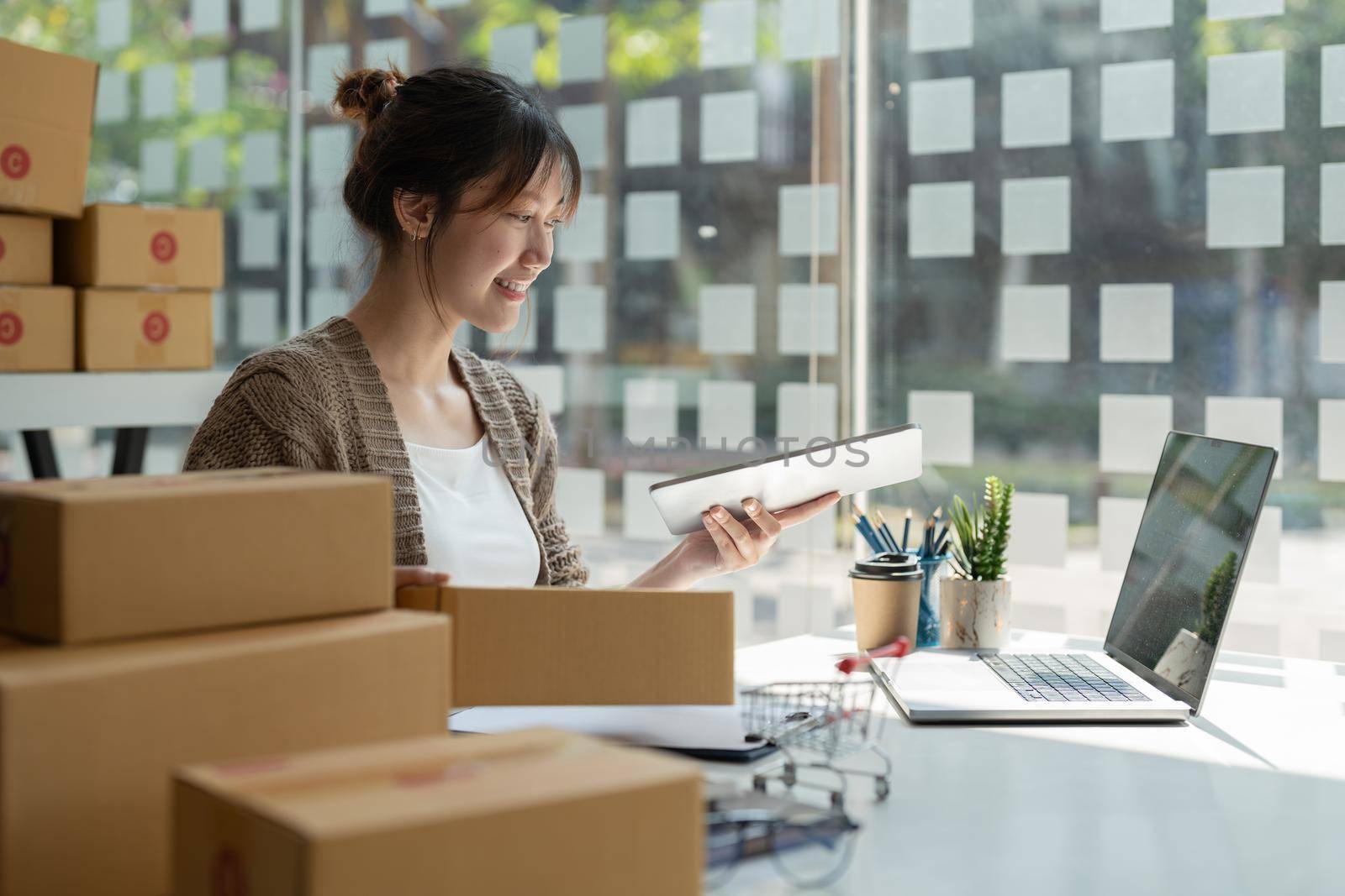 Sell online, Young asian woman checking order and customer's details and addresses on laptop or box in order to prepare for shipping according to the information, Online shopping SME entrepreneur.